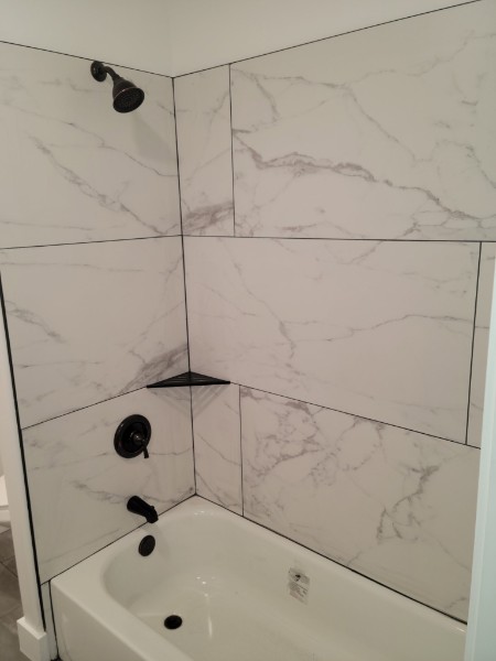 Marble-look tile around a bathtub with black fixtures