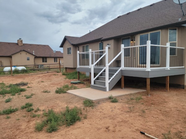 Small deck beside a tan stucco house with white posts and black balusters.