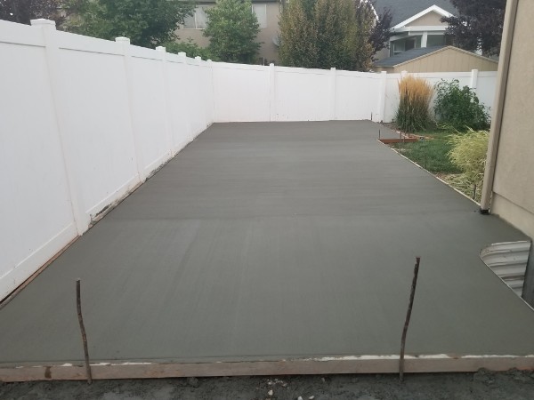 Fresh concrete slab between the house and white vinyl fence.