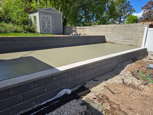 Raised fresh slab between dark block walls and gray X-door shed.