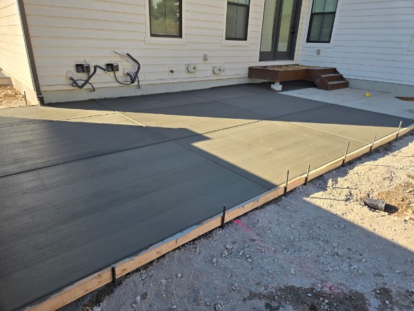 Fresh broom-finish patio at white horizontal siding with dark glazed doors and timber step.